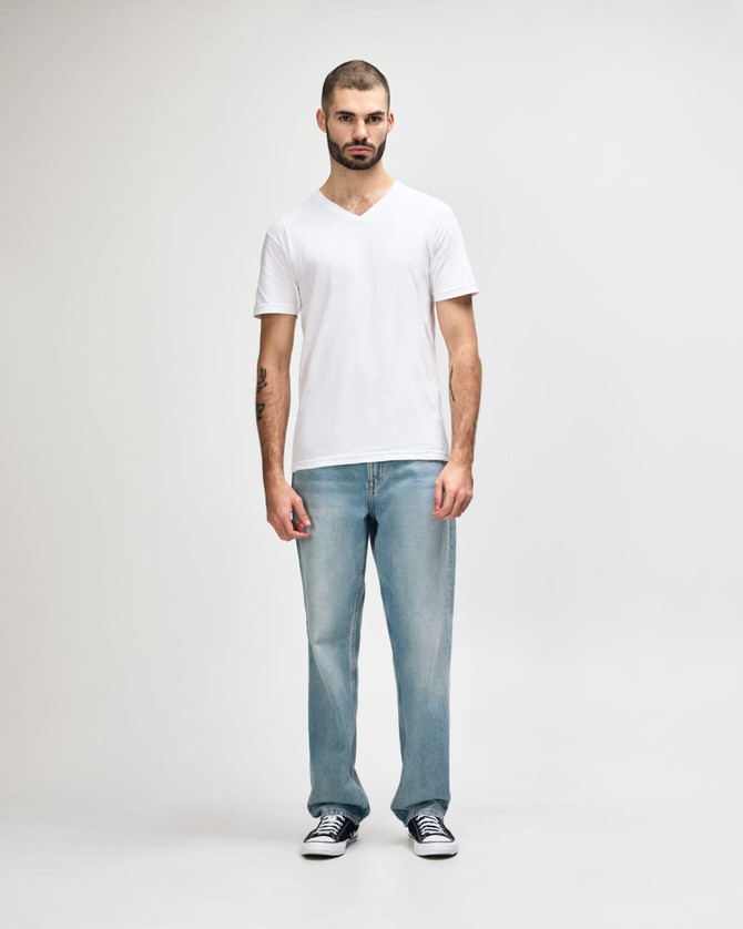 A white Gildan Softstyle adult V-neck T-shirt on a male model, paired with dark denim jeans. The shirt has a logo.