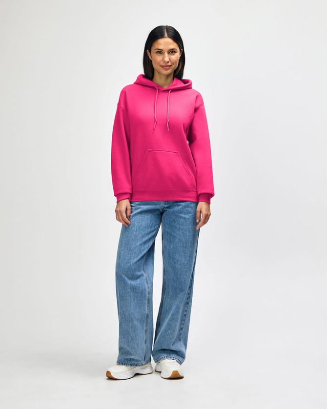 A young man wearing a bright pink hooded sweatshirt and black jeans, standing with hands in pockets. The sweatshirt features a logo.
