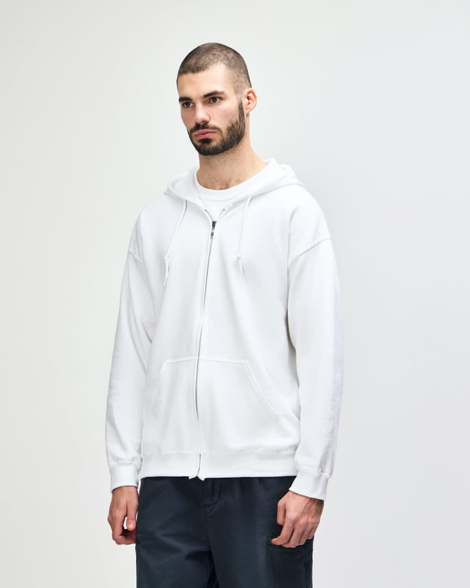 A white Gildan Heavy Blend adult full zip hooded sweatshirt is displayed on a model. The sweatshirt features a hood and a relaxed fit.