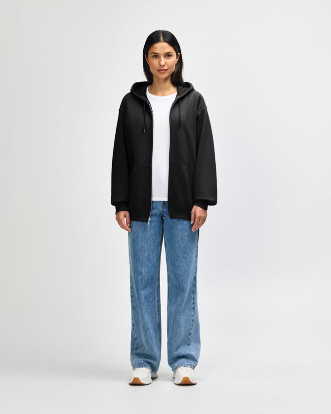 A model wearing a black Gildan Heavy Blend Adult Full Zip Hooded Sweatshirt, paired with black pants and sneakers.