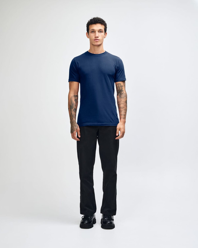 A model wearing a navy unisex fine jersey short sleeve t-shirt and tan wide-leg pants. The t-shirt has a logo.