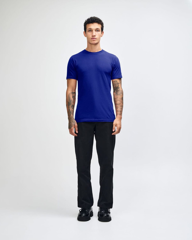 A unisex fine jersey short sleeve T-shirt in navy blue, worn by a model with curly hair, paired with beige pants.