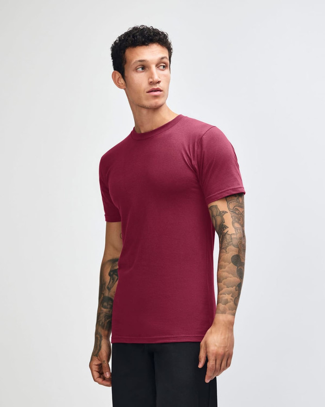 A unisex fine jersey short sleeve t-shirt in burgundy, featuring a logo, displayed on a male model from the side.