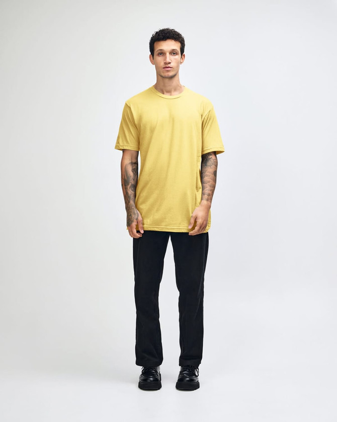 A model wearing a yellow unisex fine jersey short sleeve t-shirt and loose blue denim jeans, hands in pockets.