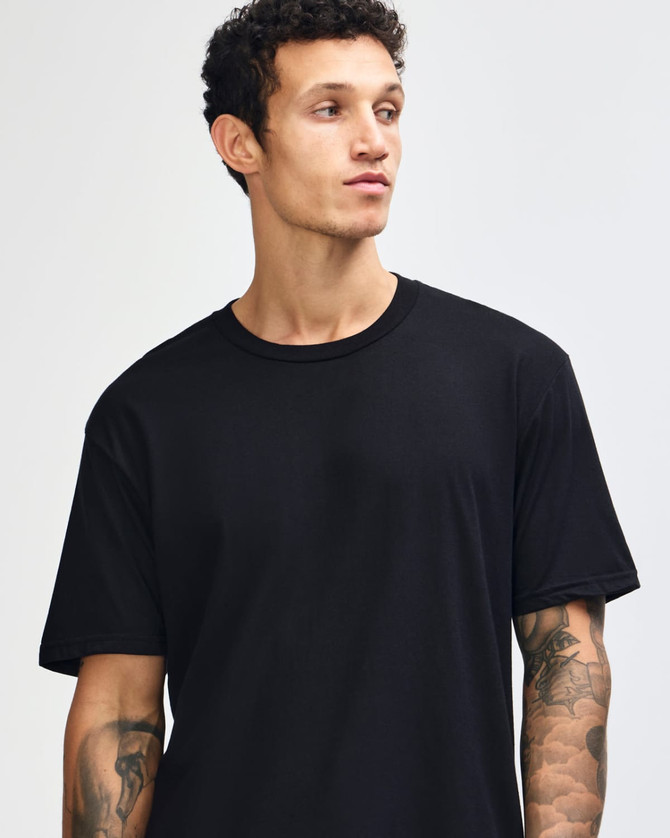 A black unisex short sleeve t-shirt is worn by a model, paired with light blue jeans and white shoes.