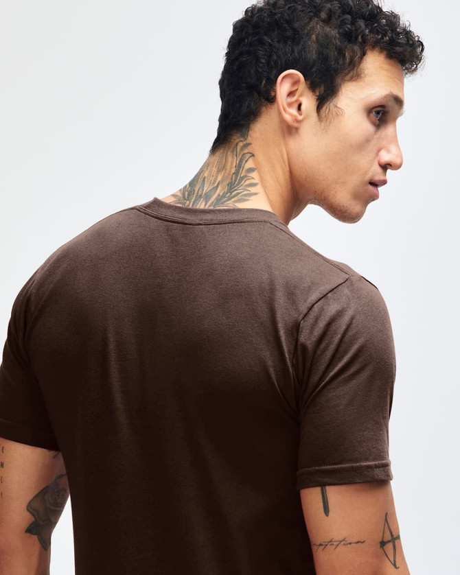 A brown short sleeve T-shirt with a fitted design, featuring a logo on the back. The model has tattoos visible.