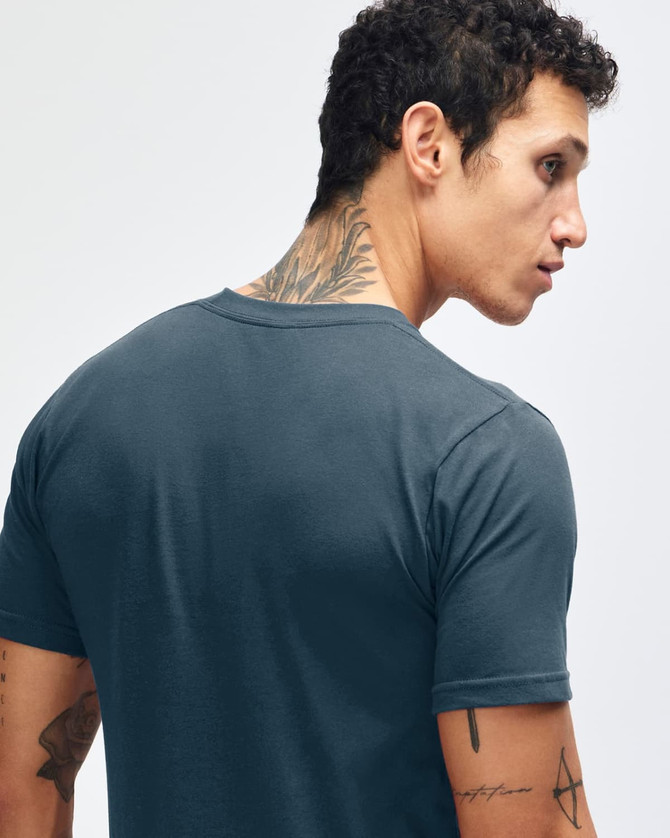 A model wearing a navy unisex fine jersey short sleeve T-shirt paired with black trousers and white shoes.