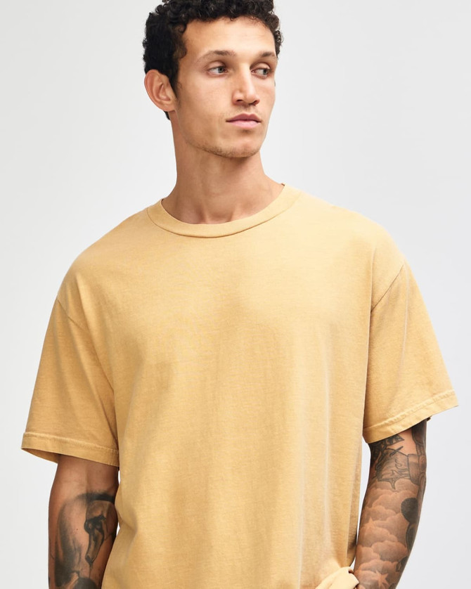 A unisex garment dyed heavyweight cotton t-shirt in a soft mustard colour, featuring a relaxed fit and a logo.