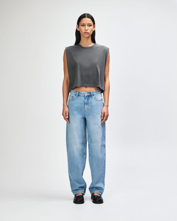A grey women's muscle t-shirt paired with light blue baggy jeans and black and white sneakers.