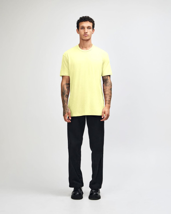 A man wearing a bright yellow unisex short sleeve t-shirt and black baggy pants, with sneakers.