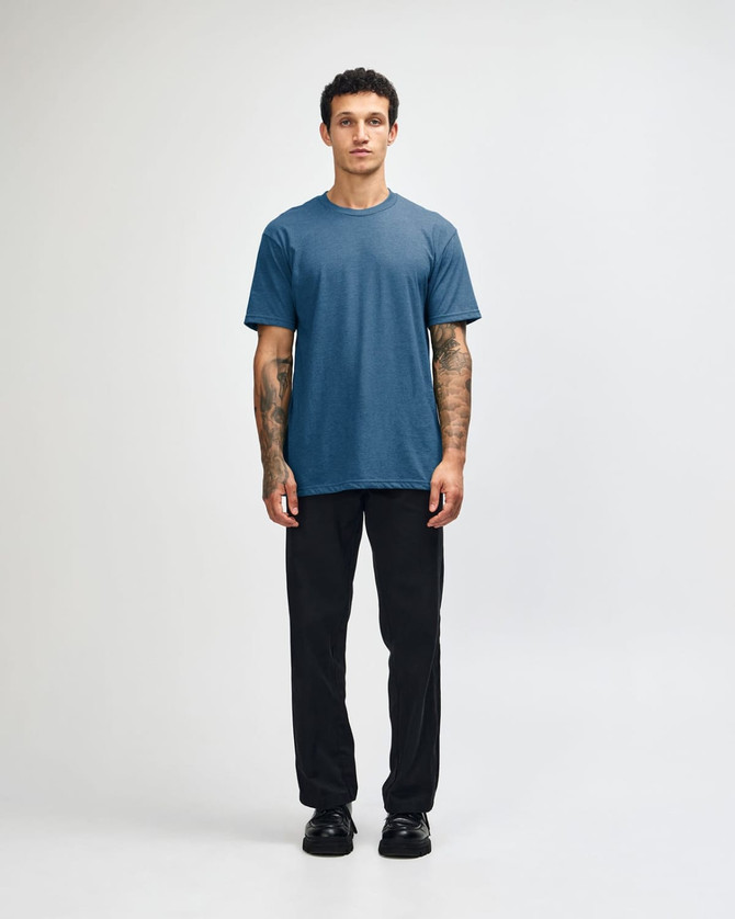 A unisex CVC short sleeve t-shirt in a blue shade, paired with black cargo pants. The model stands casually.