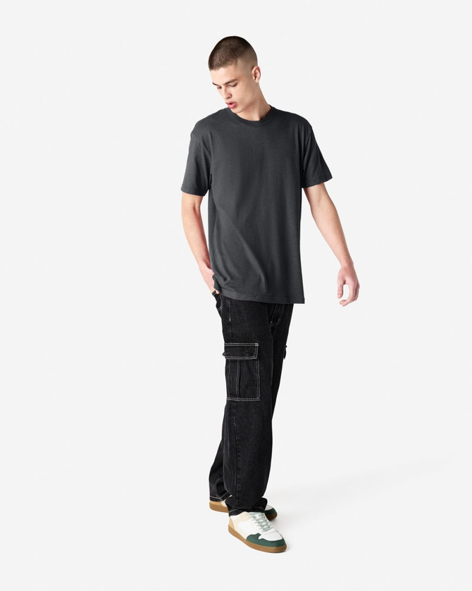 A model is wearing a dark grey unisex CVC short sleeve t-shirt paired with black cargo pants and sneakers.