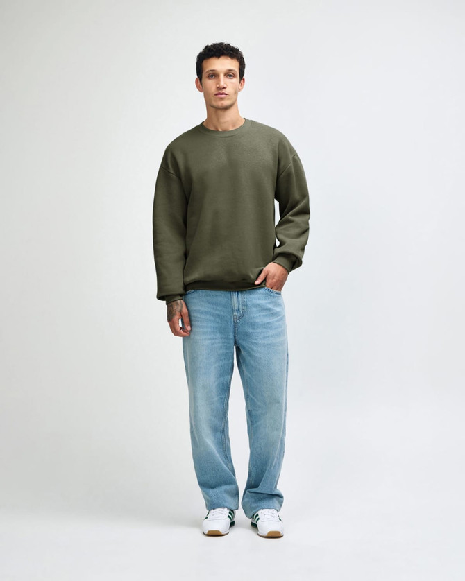 A unisex crewneck sweatshirt in olive green, paired with black cargo pants, worn by a model. Features a logo.