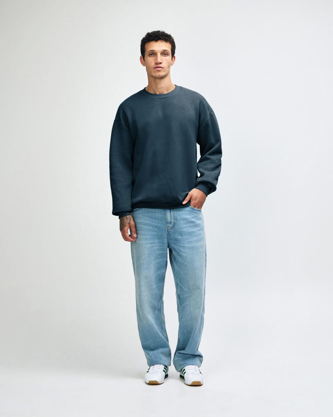 A unisex crewneck sweatshirt in a deep teal colour, paired with light blue cargo pants and styled on a model.
