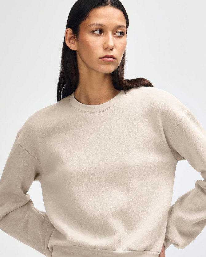 A cream women's crewneck sweatshirt with a casual fit, modelled by a woman. Featuring long sleeves and a simple design.