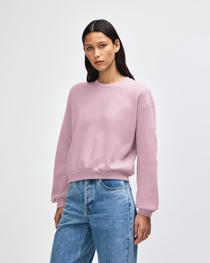 A woman wearing a pink American Apparel Reflex Fleece women's crewneck sweatshirt paired with blue jeans.