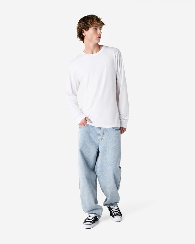 A long sleeve white T-shirt worn by a person with light blue jeans and black sneakers, featuring a logo.