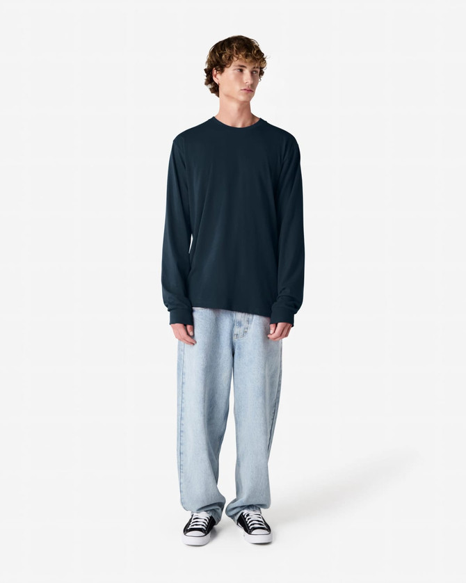 A model wearing a dark navy long sleeve t-shirt and light blue baggy jeans, standing against a plain background.