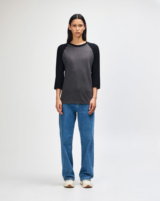 A unisex raglan t-shirt in dark grey with black sleeves, paired with light blue cargo pants. It features a logo.