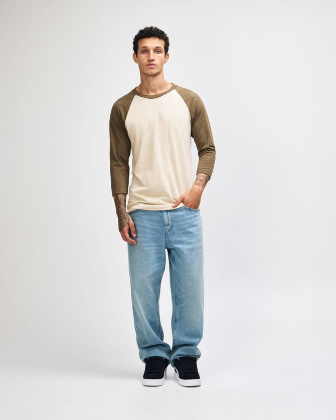 A unisex raglan T-shirt in cream with brown sleeves, paired with light blue cargo pants. Features a logo.