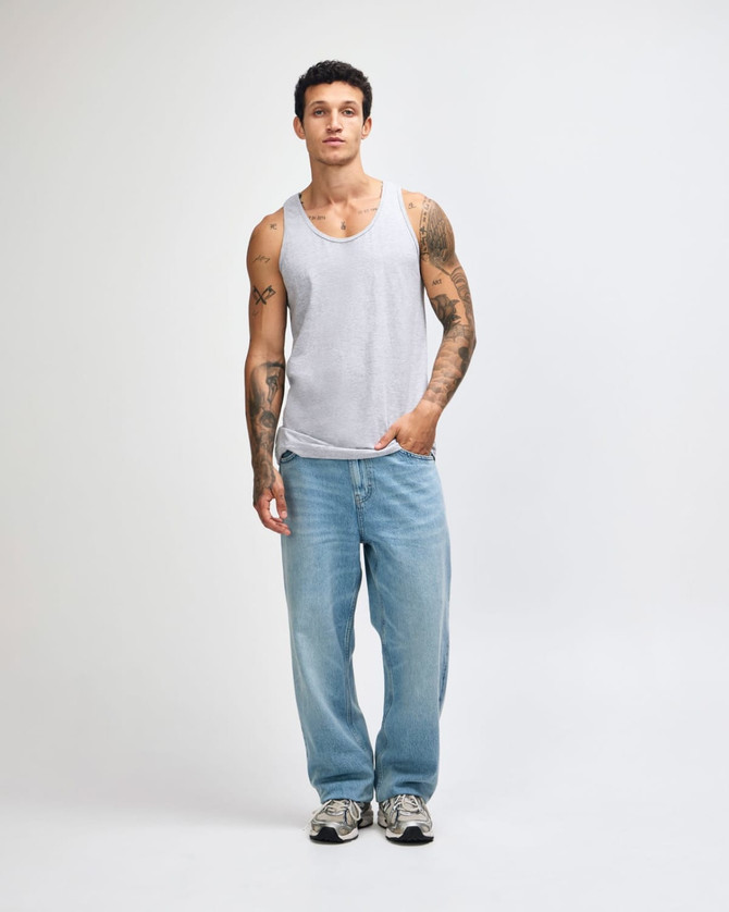 A unisex fine jersey tank in grey, paired with loose-fitting light blue jeans and black shoes. Features a logo.