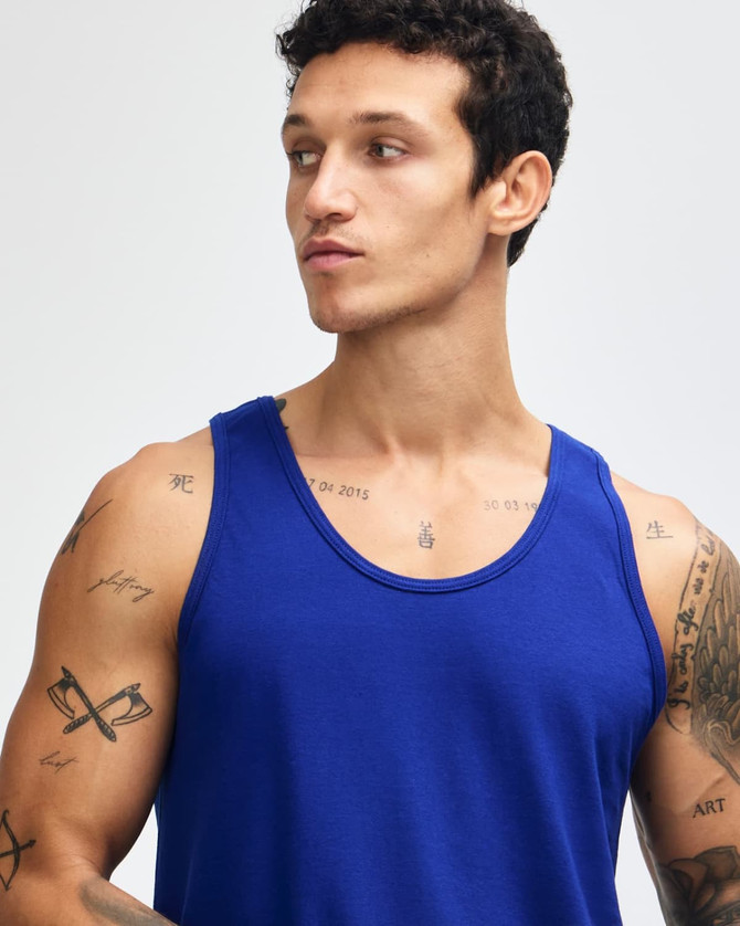 A blue unisex fine jersey tank top with a relaxed fit and no sleeves, being modelled by a person.