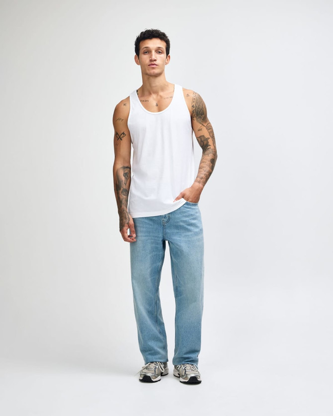 A model wearing a white unisex fine jersey tank top paired with dark cargo pants and sneakers.