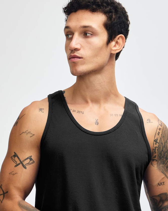 A black unisex fine jersey tank top being worn by a model, featuring a logo on the fabric.