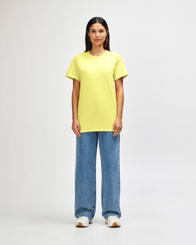 A man wearing a bright yellow Gildan Heavy Cotton adult T-shirt paired with blue jeans. The shirt has a logo.