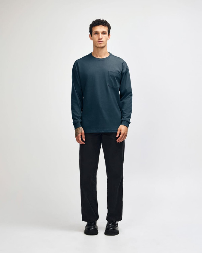 A model wears a navy long-sleeve T-shirt with a pocket, paired with olive green cargo pants and sneakers.