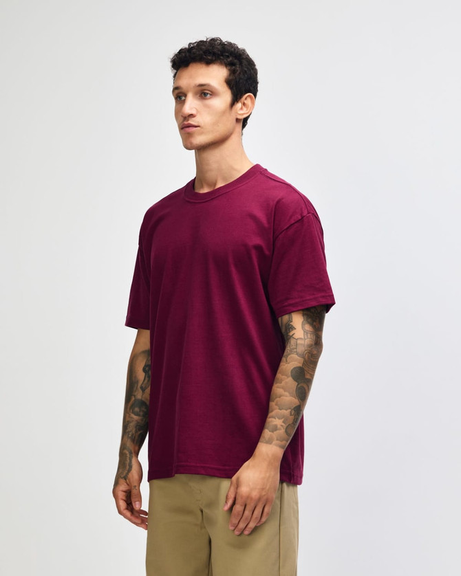 A maroon heavyweight t-shirt on a model, featuring a rounded neckline and short sleeves, with a logo present.