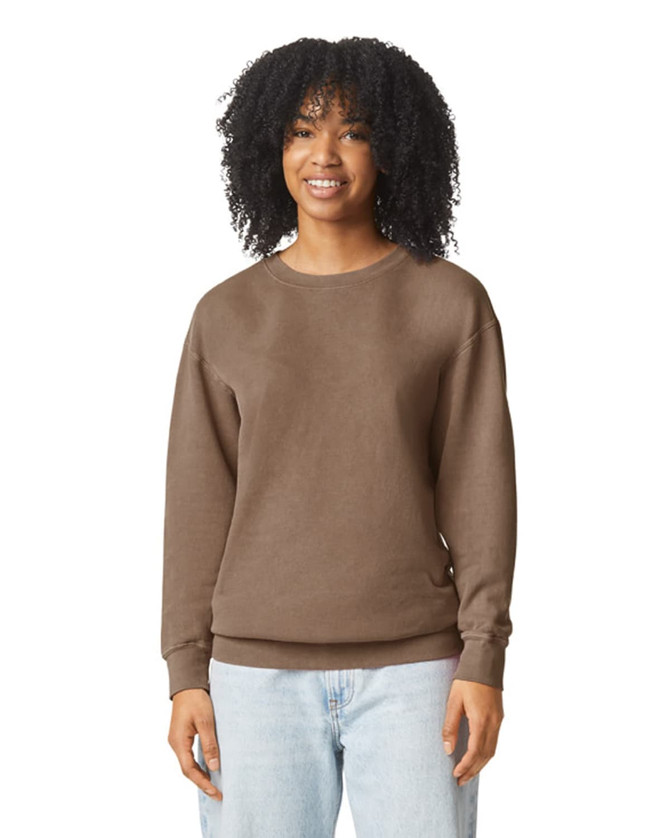A brown crewneck sweatshirt featuring a relaxed fit. The model has curly hair and is smiling. The sweatshirt has a logo.