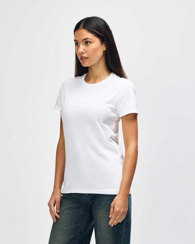 A white Gildan Heavy Cotton Ladies' T-Shirt displayed on a model, paired with blue jeans. The shirt has a simple design and a logo.