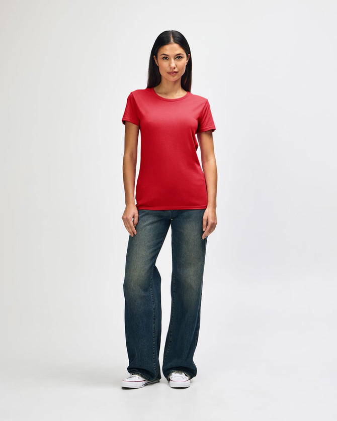 A red Gildan Heavy Cotton Ladies' T-Shirt displayed on a model wearing blue jeans and white sneakers, with a logo present.