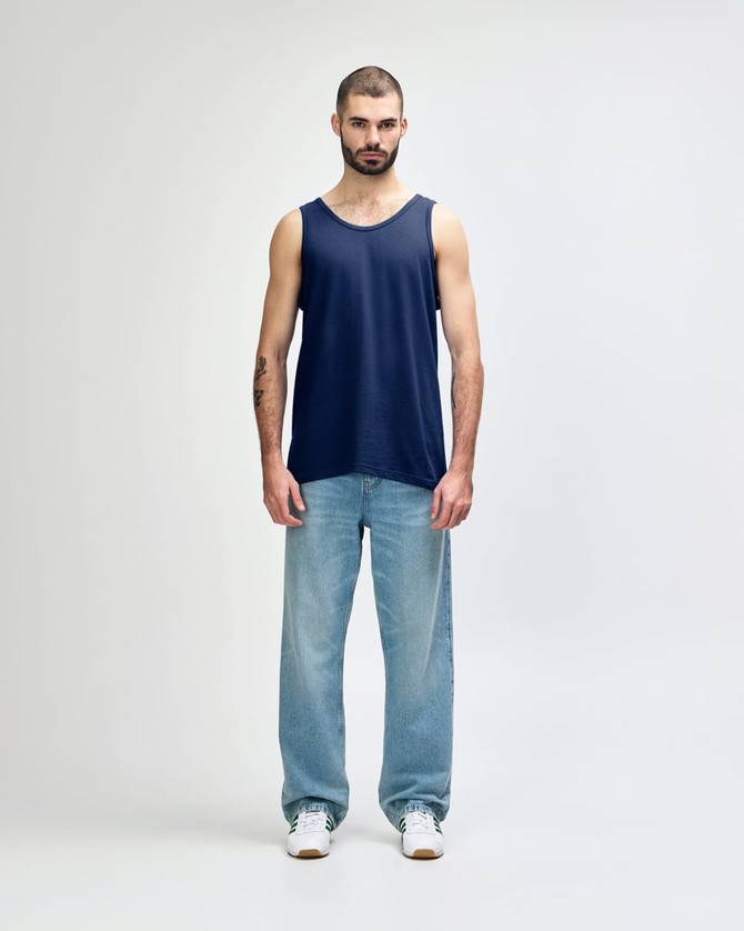 A navy blue adult tank top displayed on a male model, paired with black pants and sneakers. The top features a logo.
