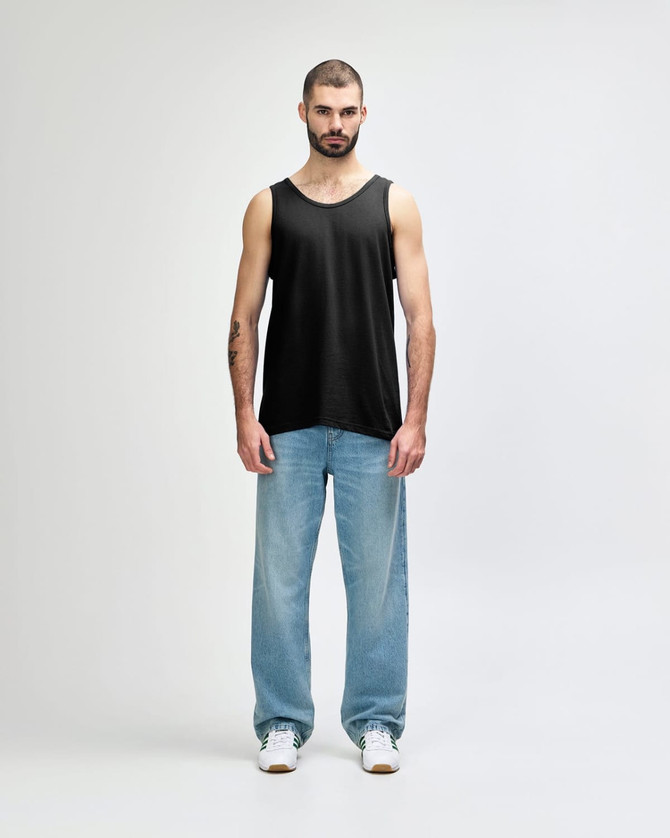 A black Gildan Heavy Cotton adult tank top worn by a model, paired with black trousers and sneakers.