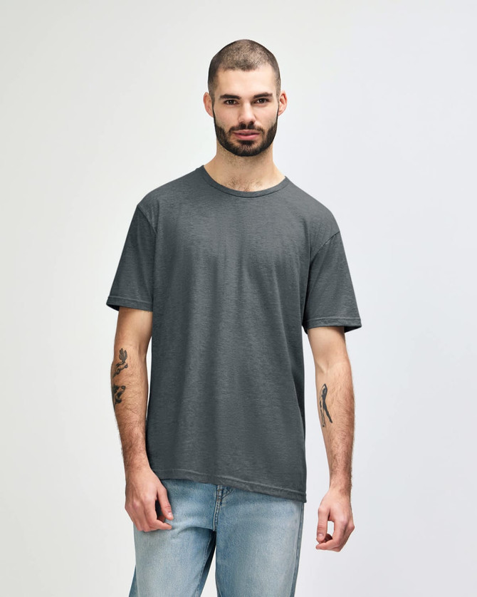 A man wearing a dark grey Gildan Softstyle adult T-shirt, paired with light blue jeans. The t-shirt has a logo.