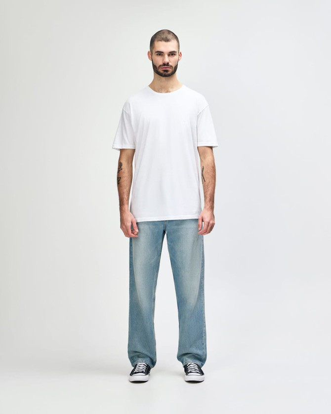 A man stands wearing a plain white Gildan Softstyle adult T-shirt paired with light blue jeans.