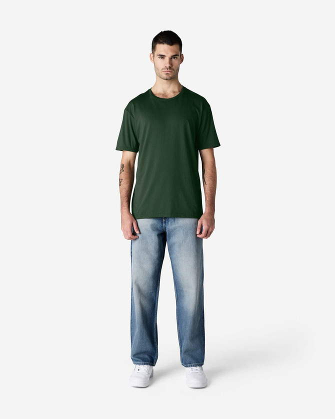 A green Gildan Softstyle adult T-shirt displayed on a model, paired with blue jeans and white shoes.