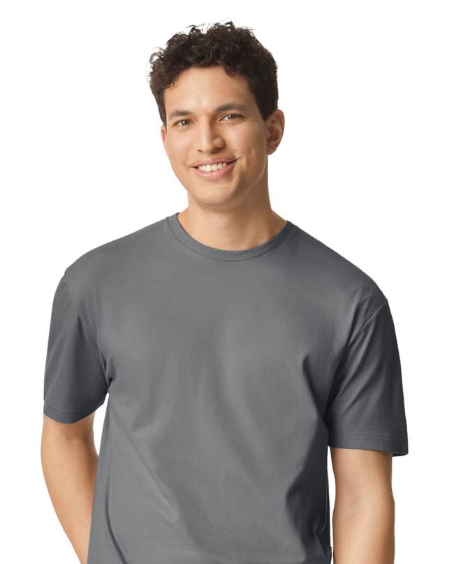 A grey Gildan Softstyle adult t-shirt displayed on a smiling male model, with a simple logo on the shirt.