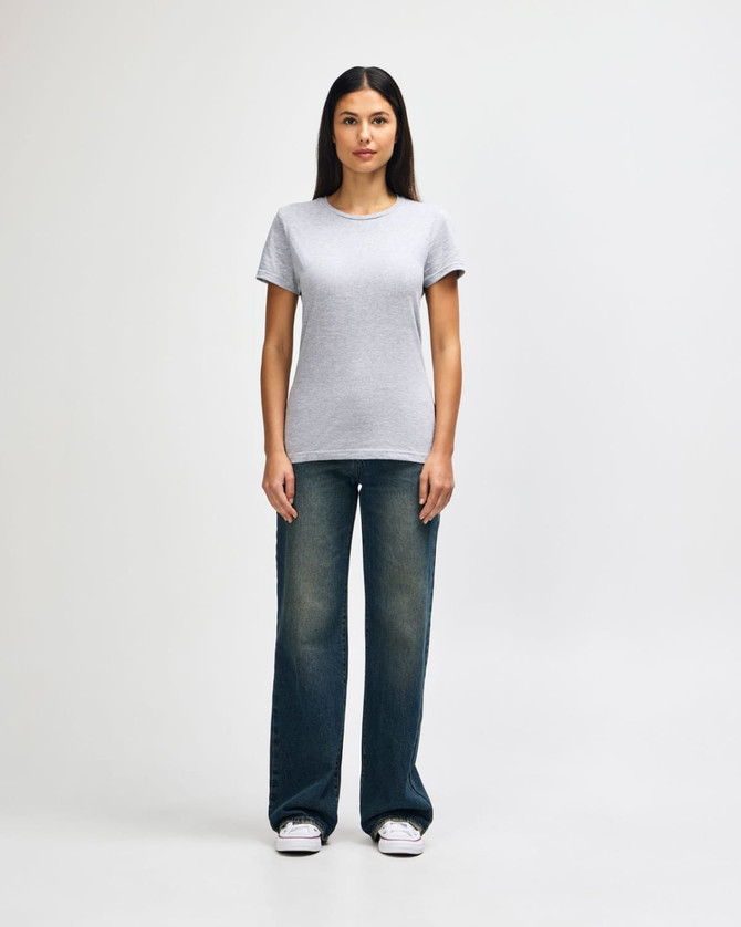 A grey ladies' t-shirt is worn with blue jeans and white sneakers, showcasing a casual outfit. The t-shirt has a logo.