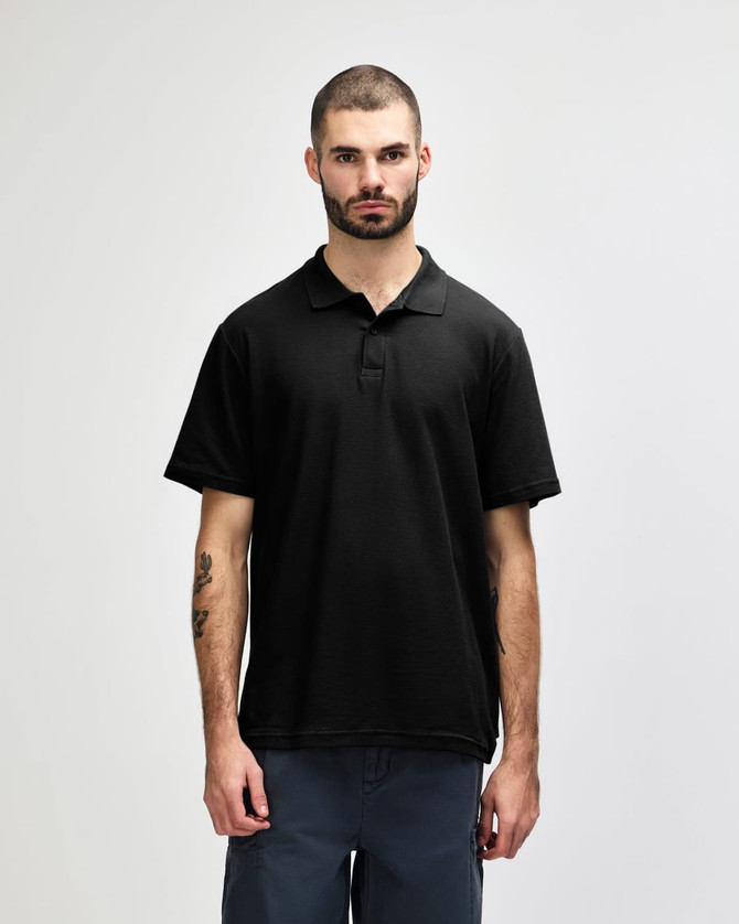 A model wearing a black Gildan Softstyle Adult Double Pique Polo with a logo on the chest.