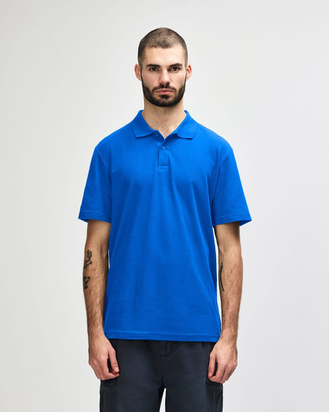 A plain blue Gildan Softstyle adult double pique polo worn by a standing male model with short hair.