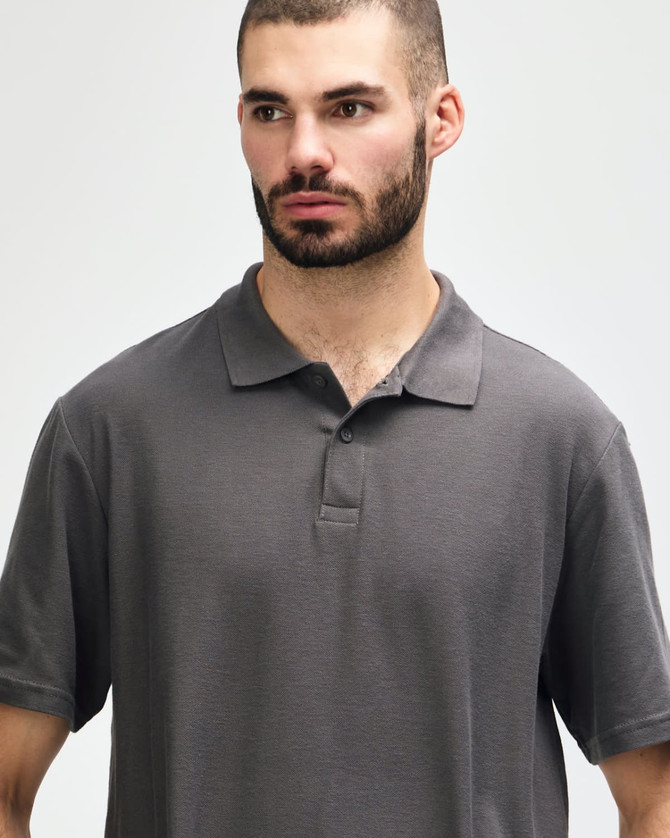 A model wearing a dark grey Gildan Softstyle Adult Double Pique Polo, featuring a classic collar and three-button placket.