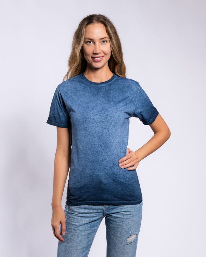 A woman poses in a navy blue Colortone® oil wash T-shirt, paired with denim jeans. The shirt has a soft, textured look and has a logo.