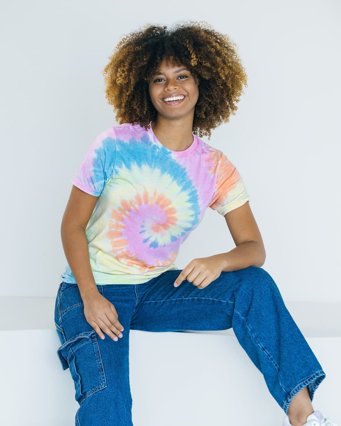 A tie dye adult t-shirt featuring pastel shades of pink, blue, yellow, and orange, displayed by a model.