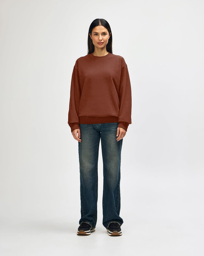 A brown Gildan Softstyle adult sweatshirt is worn by a model, paired with black pants and sneakers.