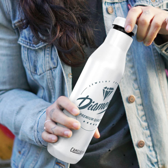 A drink bottle in white with a black lid, featuring a logo, held by a person wearing a denim jacket.