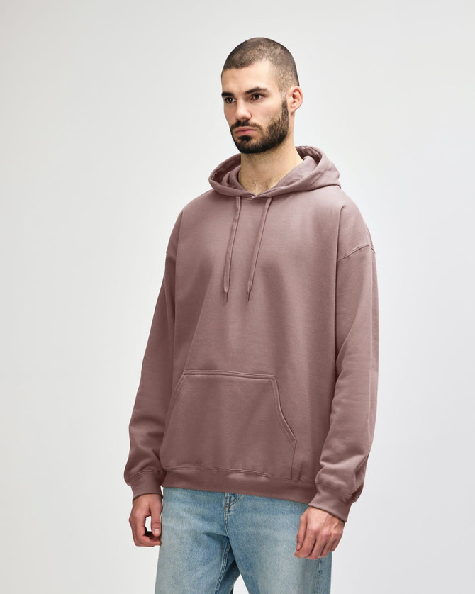 A person stands wearing a pink hooded sweatshirt with a front pocket and a drawstring hood.