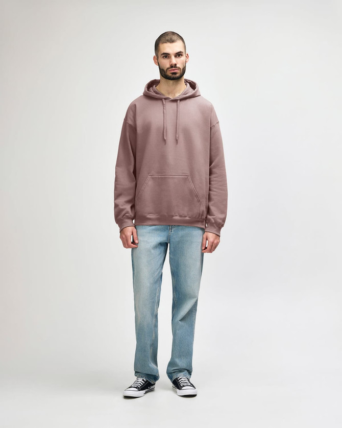 A woman wearing a dusty rose hooded sweatshirt paired with blue jeans and white shoes. The sweatshirt has a logo.
